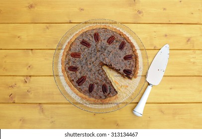 First slice removed from pecan pie on a glass plate, with a dirty pie server beside