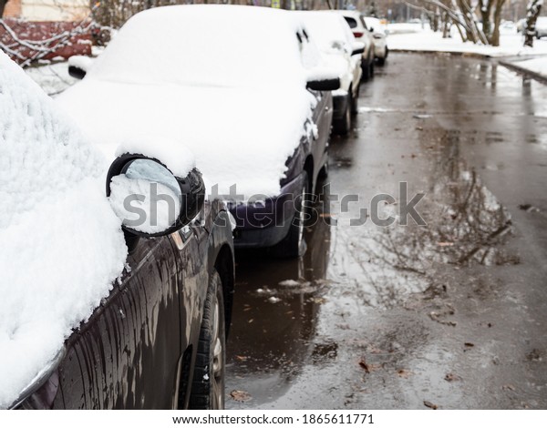 the\
first snow on cars parked along wet city road on cold autumn day\
(focus on outside side-view mirror of first\
car)