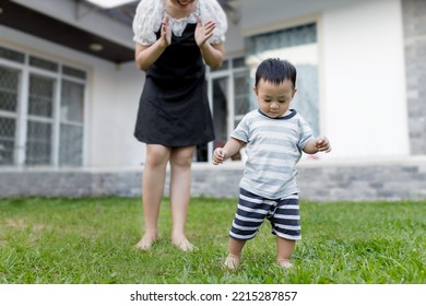 The First Step Little Baby Learning To Walk With A Happy Mother In The Front Yard. Cute Asian Baby Boy Walking.