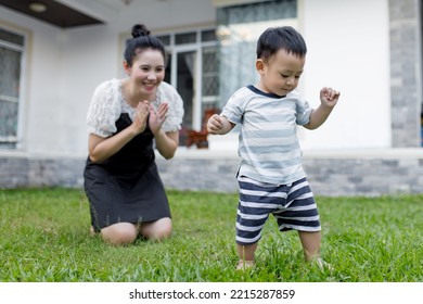 The First Step Little Baby Learning To Walk With A Happy Mother In The Front Yard. Cute Asian Baby Boy Walking.