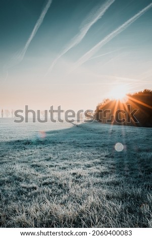 First sunlight on a early cold winter morning with frozen grass landscape and bright foggy glow. Misty winter morning with orange sunrise countryside landscape