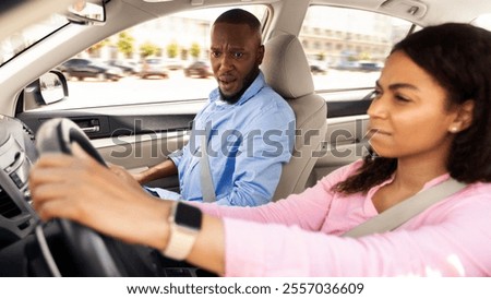First time driver sitting inside car watching road, scared male looking at serious focused black lady, woman having low skills taking exam for license at training school or riding with husband