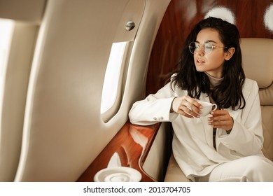 For the first time since quarantine, a young women delegate flies to a business meeting, looking out the window and drinking coffee on board the plane. Travel after covid pandemic