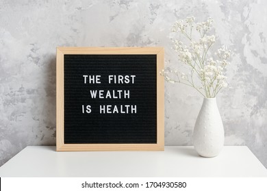 The first wealth is health. Motivational quote on letter board and bouquet of flowers gypsophila in vase on table against stone gray wall. Concept Health Care, inspirational quote of the day.
