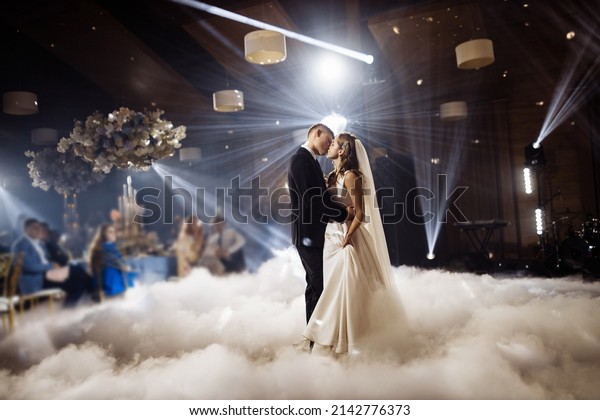 First wedding dance of newlyweds. Just married\
wedding couple dancing in darkness. Groom holds bride\'s hand\
dancing with her in the middle of restaurant. Happy bride and groom\
and their first dance