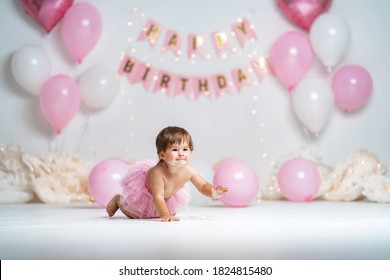 First year's birthday.a happy little girl in a pink tutu skirt crawls on a background with garlands and pink balloons, celebrating her first birthday. Birthday decoration.