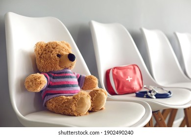 First-aid kit, stethoscope and cute teddy bear on white chairs in waiting room of children's medical center or pediatric clinic. Concept of kids' visit to hospital to see pediatrician or family doctor