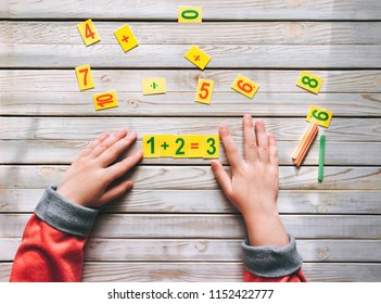 First-grader learn to count. The child decides a mathematical example. 1 + 2 = 3. Basic knowledge.