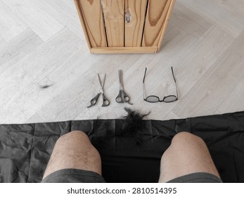 First-person perspective capturing the messy aftermath of a home haircut, featuring cut hair, scissors, and glasses on the floor.