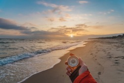 First-person View Of A Female Hand With A Compass On A Background Of A Beautiful Sea Landscape. The Concept Of Navigating The Search For Your Own Path And Orientation To The Cardinal Points
