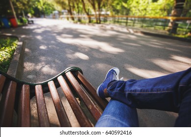 First-person view a man sitting on wooden bench in the park.