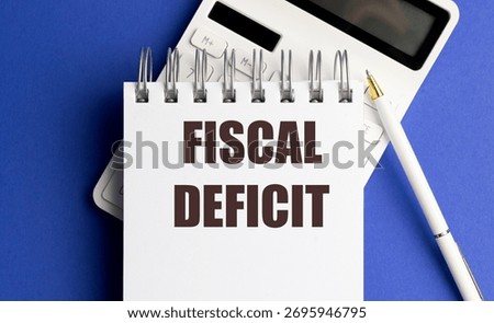 Fiscal deficit text on notebook with a calculator and pen on blue background, concept of budget shortfall. 