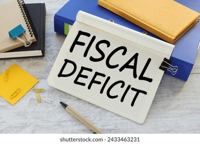 FISCAL DEFICIT text on a notepad near a blue folder with a yellow notepad