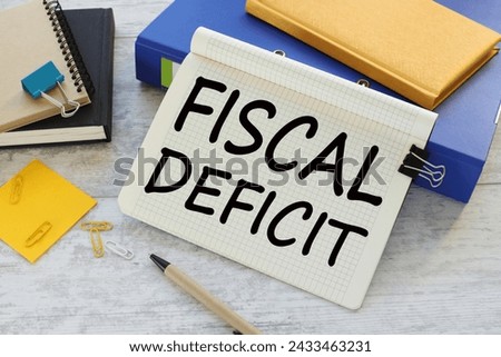 FISCAL DEFICIT text on a notepad near a blue folder with a yellow notepad