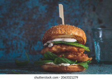 Fish burger on gray plate, dark blue background, copy space. Cod fish in batter with mayonnaise and spinach sandwich.