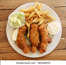 Fish & Chips. Mahi Mahi fish and chips with French fries and pineapple coleslaw on a white plate on a wooden table. Hawaiian Fish-n-Chips 