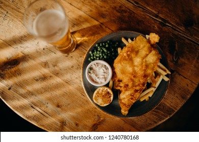 Fish And Chips Plate And Pint Of Beer On A Wooden Table Viewed From Above.