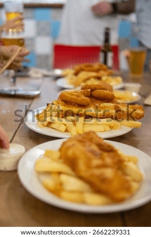 Fish and Chips served on plate, with blurred background of people holding beer glasses