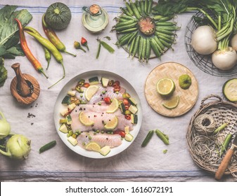 Fish cooking preparation with raw god fish fillet in white cooking pan on rustic table with various vegetables, top view.  Healthy low carb dieting food