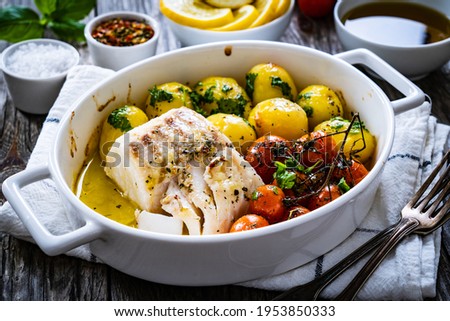 Fish dish - baked cod fillet with potatoes and cherry tomatoes on wooden table 