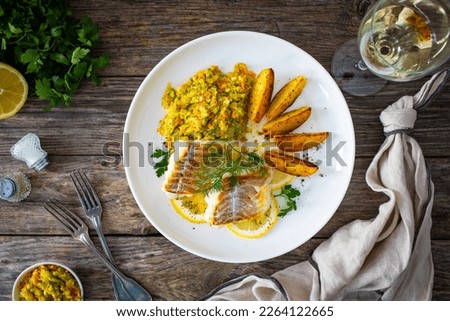 Fish dish - fried cod with baked potatoes and fresh vegetables on wooden table 