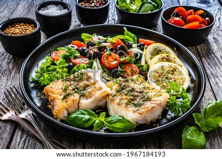 Fish dish - fried cod fillet with fresh vegetable salad on wooden table 