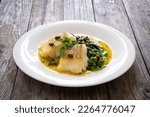 Fish dish - fried cod with spinach and capers in saffron sauce on wooden table 