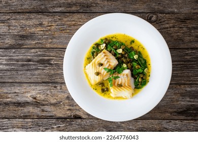 Plato de pescado - bacalao frito con espinacas y alcaparras en salsa de azafrán sobre mesa de madera 