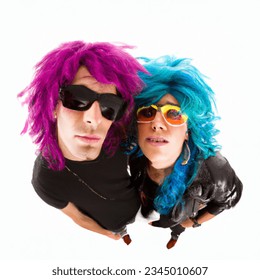 Fish eye photo of single attractive male and attractive female dressed as 80s glam rocker wearing sunglasses and big colorful punk-style wigs, white background