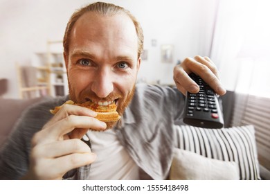 Fish Eye Portrait Of Smiling Bearded Man Watching TV At Home And Eating Pizza While Binge Watching Favorite Series, Copy Space