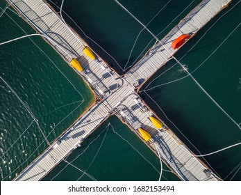 Fish Farm, Top Down Aerial Drone Image Showing Floating Platforms, Feed Pups And Piping On A Sunny Day,