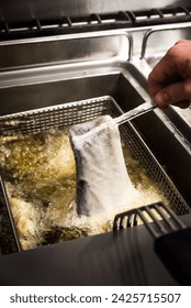 A fish fillet in batter being dipped into deep fat fryer in restaurant kitchen
