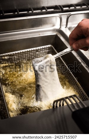 A fish fillet in batter being dipped into deep fat fryer in restaurant kitchen