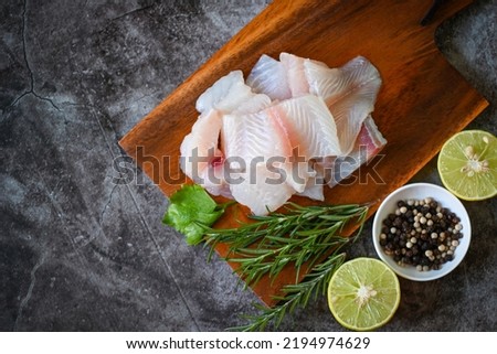 fish fillet on wooden board with ingredients for cooking, fresh raw pangasius fish fillet with herb and spices black pepper lemon lime and rosemary, meat dolly fish tilapia striped catfish - top view 