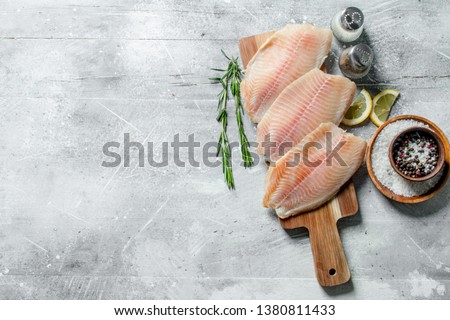 Fish fillet on a wooden cutting Board with rosemary, spices and lemon slices. On white rustic background