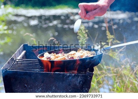 Fish is fried in frying pan by the river. Cooking fresh fish catch. Successful fishing. Delicious fish dish fried over the fire. Dish from fried fish cooked on fire. Pleasant rest by the river
