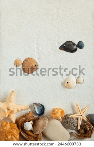 Fish made from shells and pebbles on fine sand. Imitation of the underwater world. Top view, flat lay.