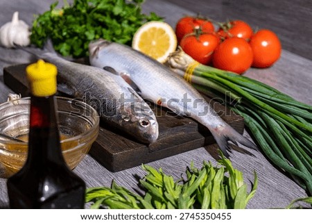 Fish menu concept. Two cleaned raw fish on cutting board surrounded by ripe tomatoes, parsley, tarragon, garlic, green onion, honey and soy sauce. Fish diet for digestive health and essential fats.