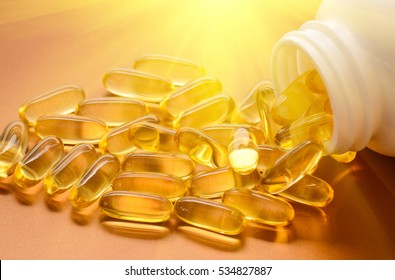 Fish oil capsules with omega 3 and vitamin D in a plastic bottle on a shiny texture with sun beams, healthy diet concept
