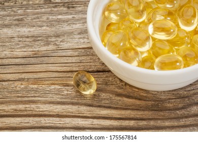 Fish Oil Capsules - A Small Ceramic Bowl On A Grained Wood