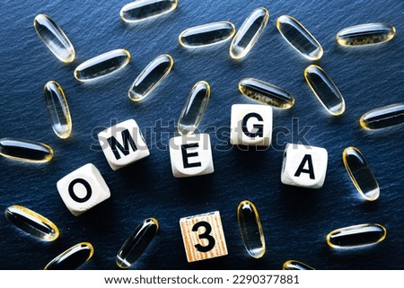 Fish oil pills and wooden cubes with inscription OMEGA 3 on a dark background, top view.