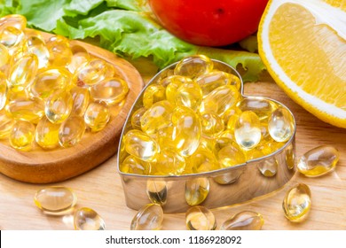 Fish Oil, Soft Capsule, Omega 3, Supplement Food Vitamin D Capsules In Heart Shaped  With Vegetables And Fruit Greens Tomato Lemon On Wood . Still Life Of Healthy Food And Supplementary  Diet Concept