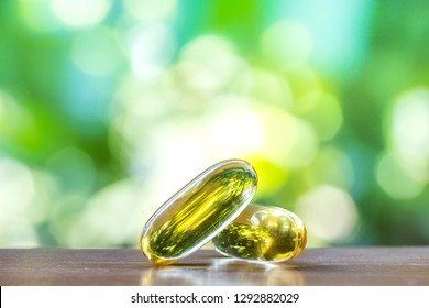 Fish Oil Supplement Capsules In Selective Focus On Top Wooden Table With Green Natural Bokeh Background