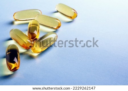 Fish oil. Yellow softgels lie on a light blue surface. Healthy lifestyle. Background with copy space for text. Softgel close up. Omega fatty acid capsule. Vitamins and supplements. Macro