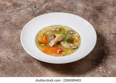 Fish soup Ukha from sturgeon. In a white, round, ceramic plate, there are two pieces of sturgeon fillet, chopped carrots and fish broth. Nearby is a small, white, ceramic bowl with finely chopped dill