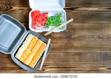 Fish Sushi Rolls With Salmon And Sesame, Ginger, Wasabi Packed In Plastic Disposable Food Container On Wooden Rustic Background. Seafood, Food Delivery Service From Restaurant Concept.