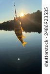 Fish that was caught by a hook or held in hand by a person on a lake with water, sunsets, the sun and sky in the background