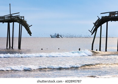 Fish Trawler Net Fishing Followed By Large Flock Of Seagulls Off Beach With Broken Wooden Fishing Pier Structure, Outer Banks, OBX, North Carolina, NC, US American Atlantic Coast