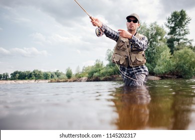 Fisherman in action. Guy is throwing spoon of fly rod in water and holding part of it in hand. He looks straight forward. Man wears special protection clothes.
