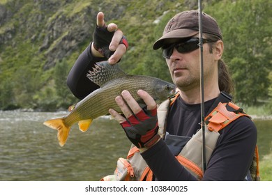 Fisherman and the catch. A fisherman in a professional outfit holding a large grayling